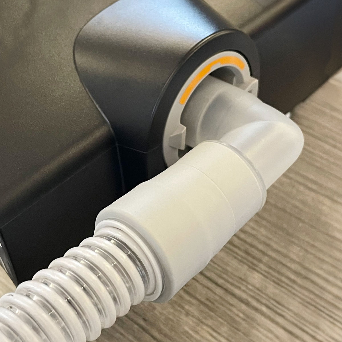 Close-up of a white hose connected to a black cpap device on a wooden surface