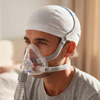 Person wearing a full-face mask and a CPAPhero hat on a white background