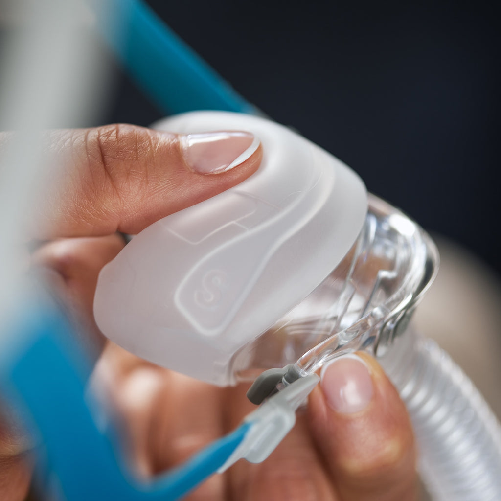 Hand holding a clear plastic mask with tubing against a dark background
