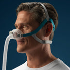 Man wearing a CPAP mask with a blue strap against a dark background