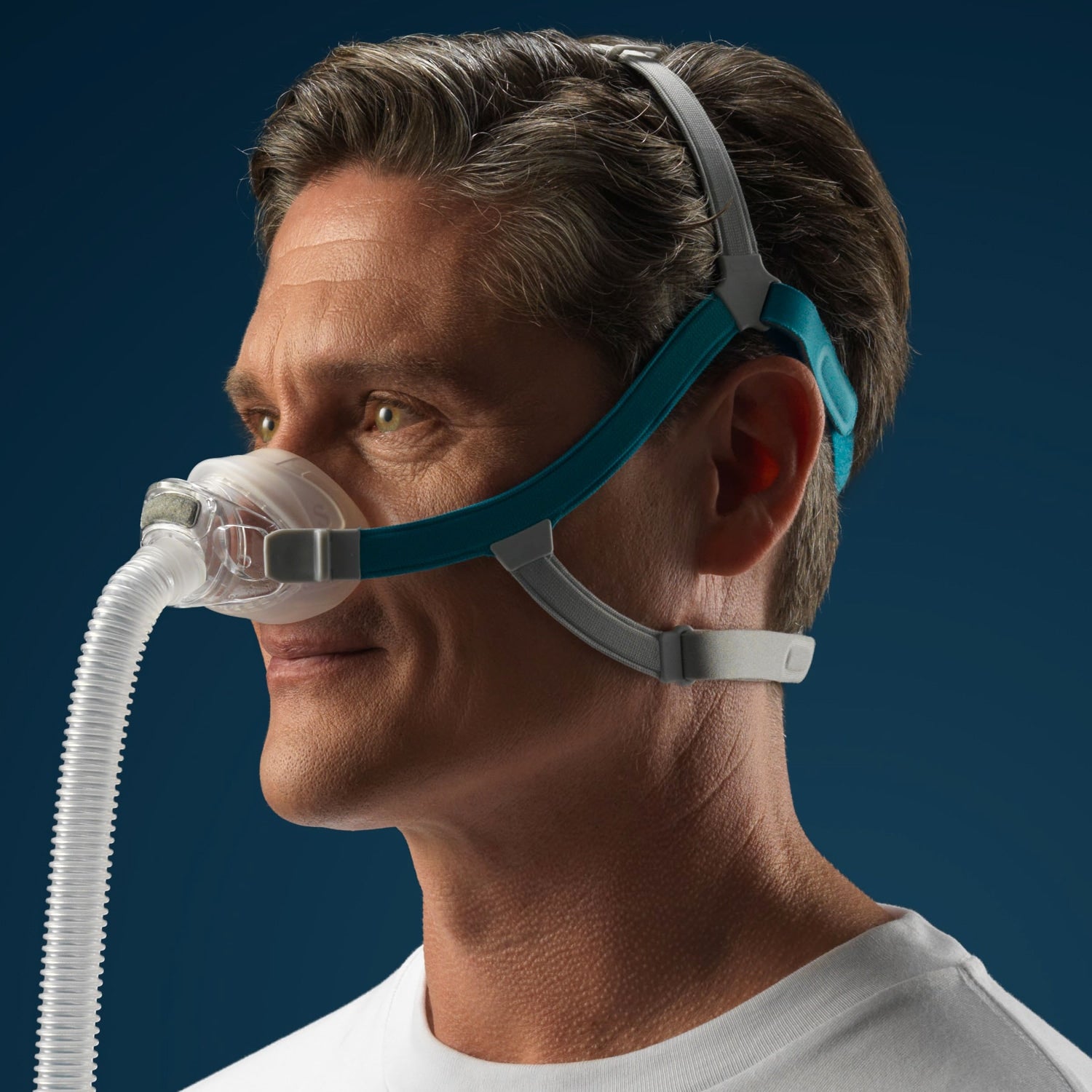 Man wearing a CPAP mask with a blue strap against a dark background