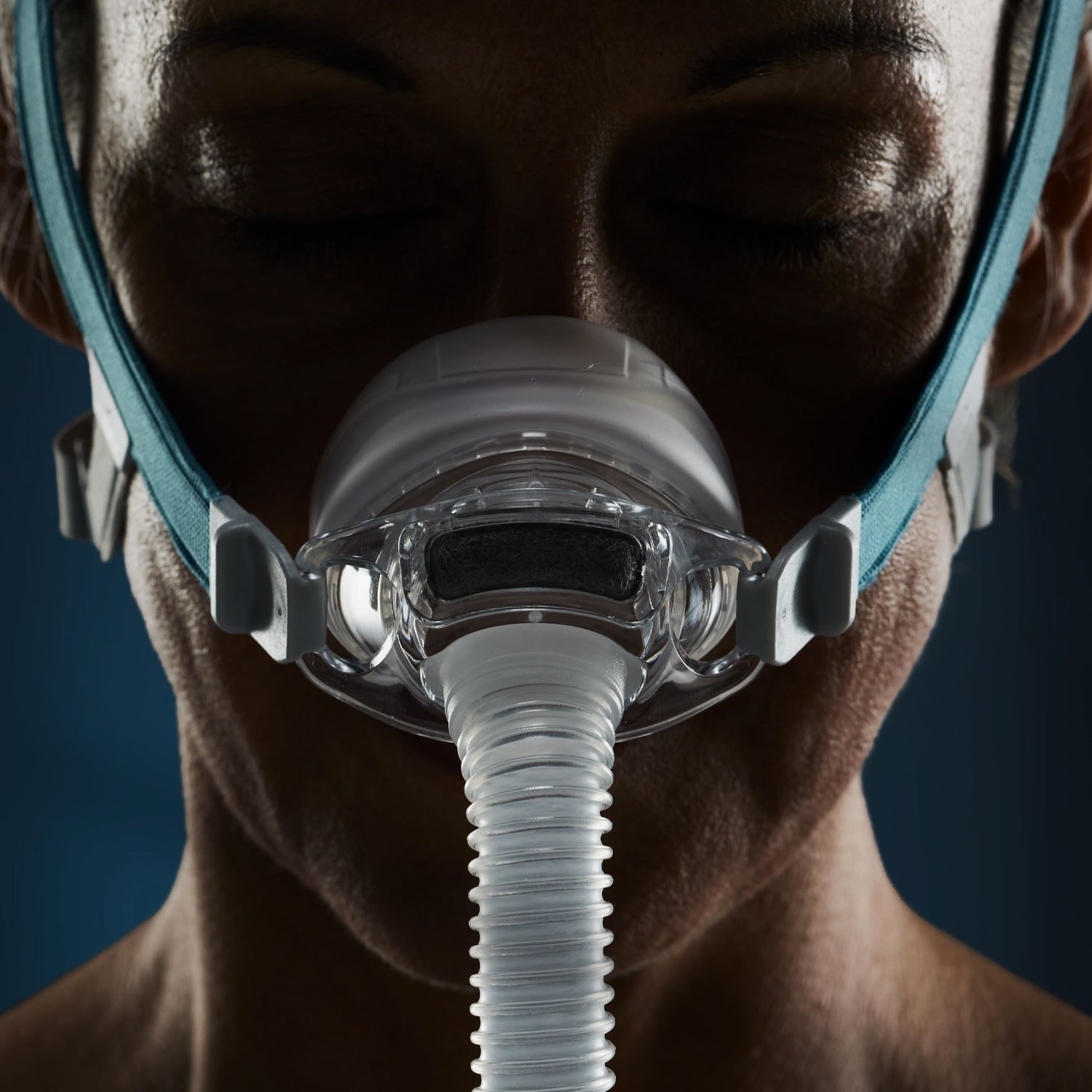 Close-up of a person wearing a CPAP mask against a dark background