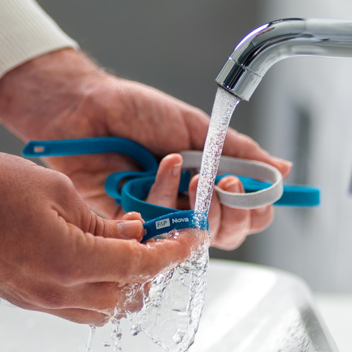 Person washing fisher paykel nova micro under running water from a faucet.