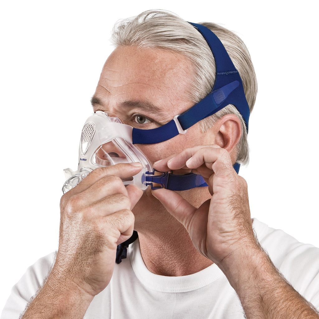Man wearing a blue and white CPAP mask on a white background