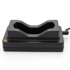 A black plastic dual-device charging dock with a curved recessed slot, featuring a small orange indicator light on the left and a power cord extending from the right, shown on a white background.