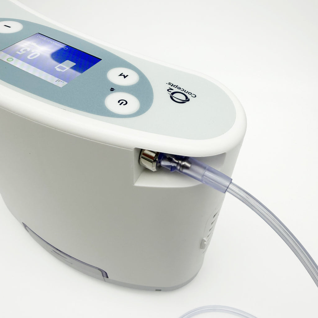 A close-up of a Liberty2 Concentrator with a digital display screen, control buttons, and a clear tubing connection, shown on a clean white background.