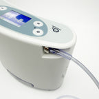A close-up of a Liberty2 Concentrator with a digital display screen, control buttons, and a clear tubing connection, shown on a clean white background.
