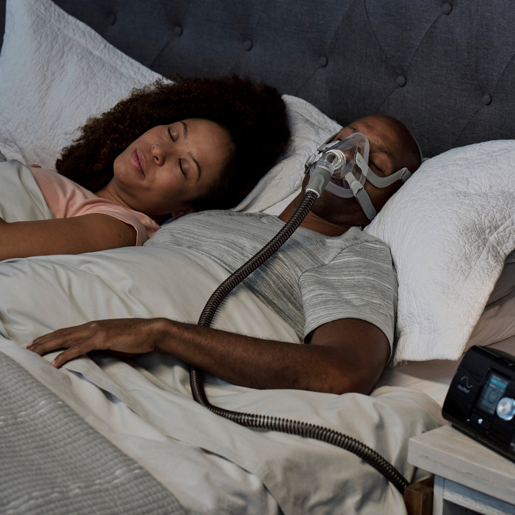 Two people sleeping in bed with a CPAP machine 