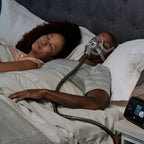 Two people sleeping in bed with a CPAP machine 
