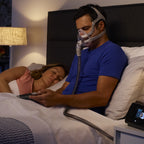 Man using a CPAP machine with a woman in bed
