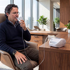 Man using an inhaler device in a modern office setting with a ResMed device on a table.