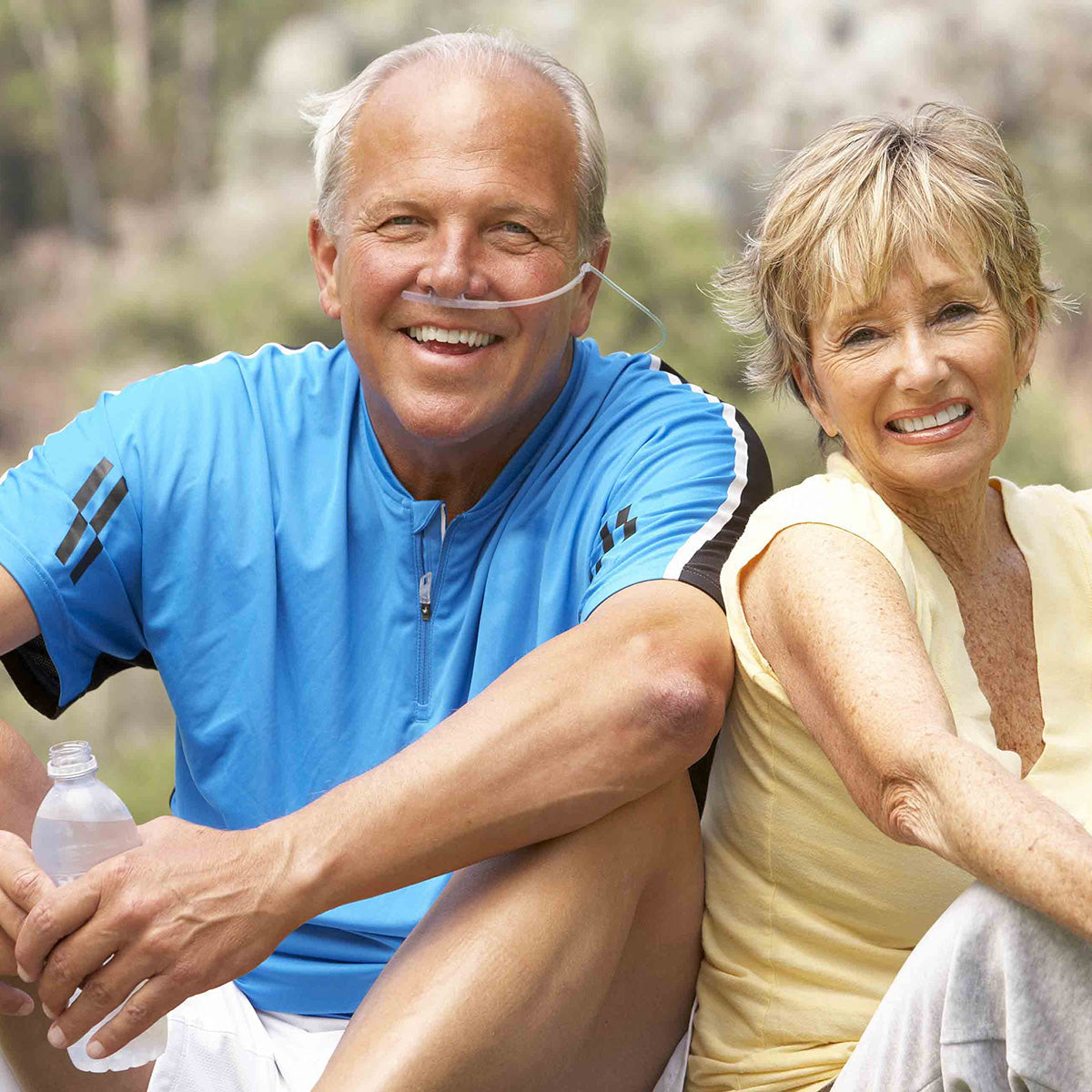 Man wearing an oxybreather single sided nasal cannula and woman sitting outdoors with a water bottle, smiling.