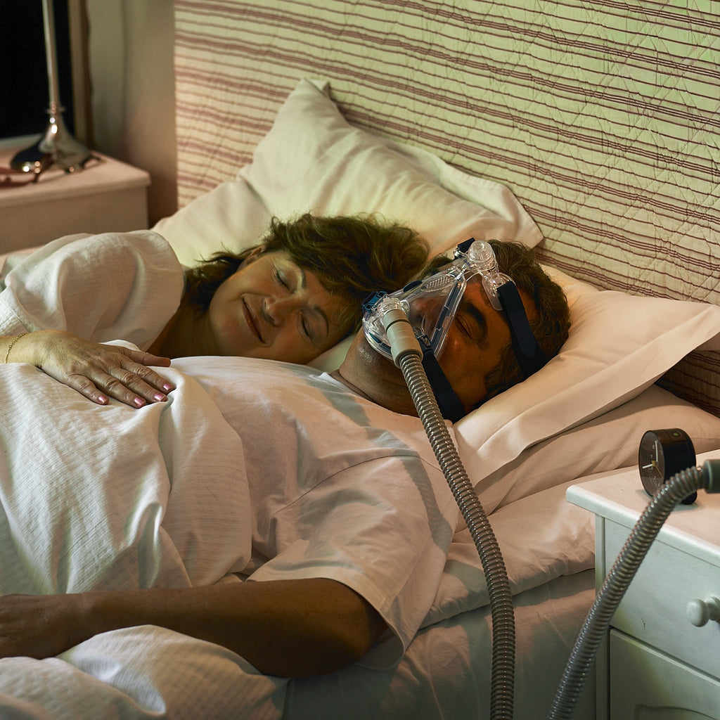 Person using a CPAP machine in bed with a partner.