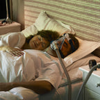 Person using a CPAP machine in bed with a partner.