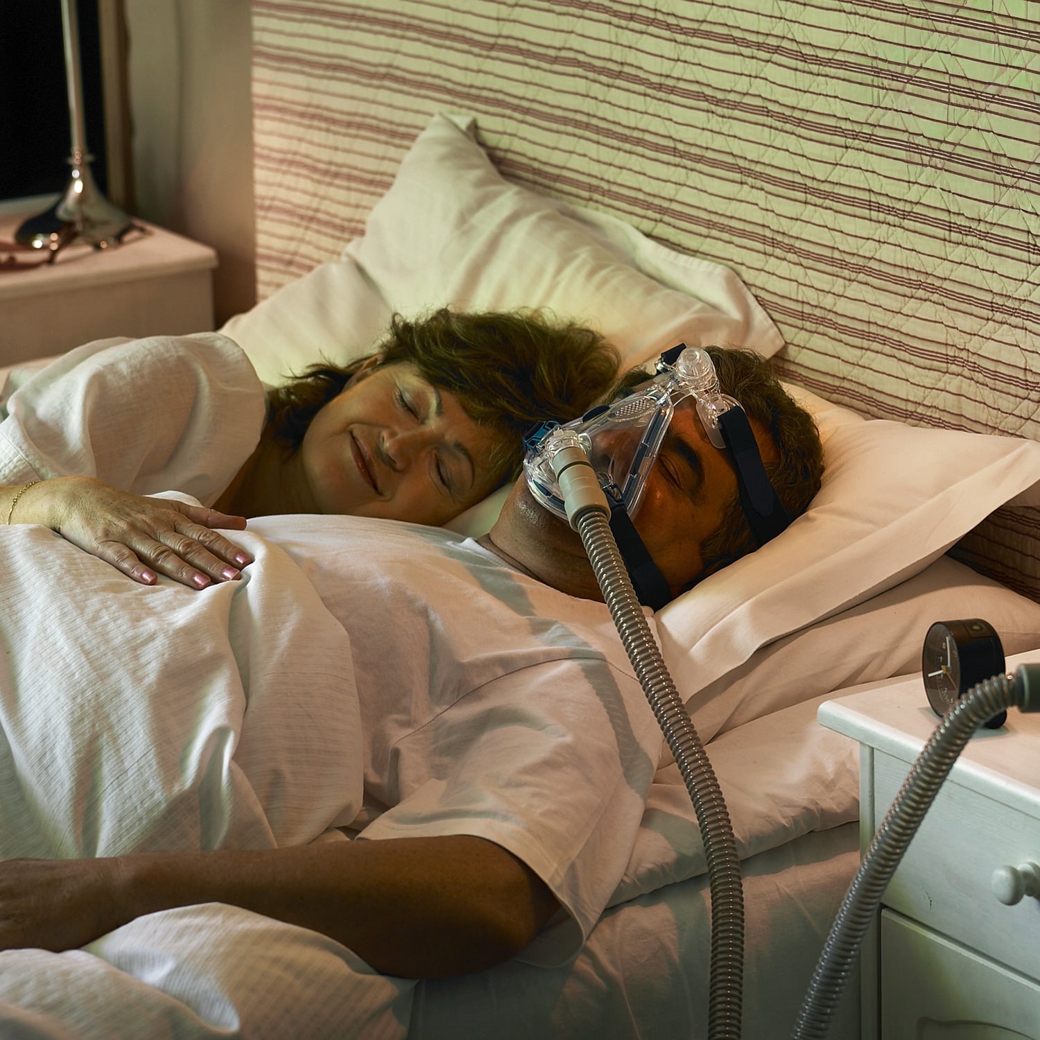 Person using a CPAP machine in bed with a partner.