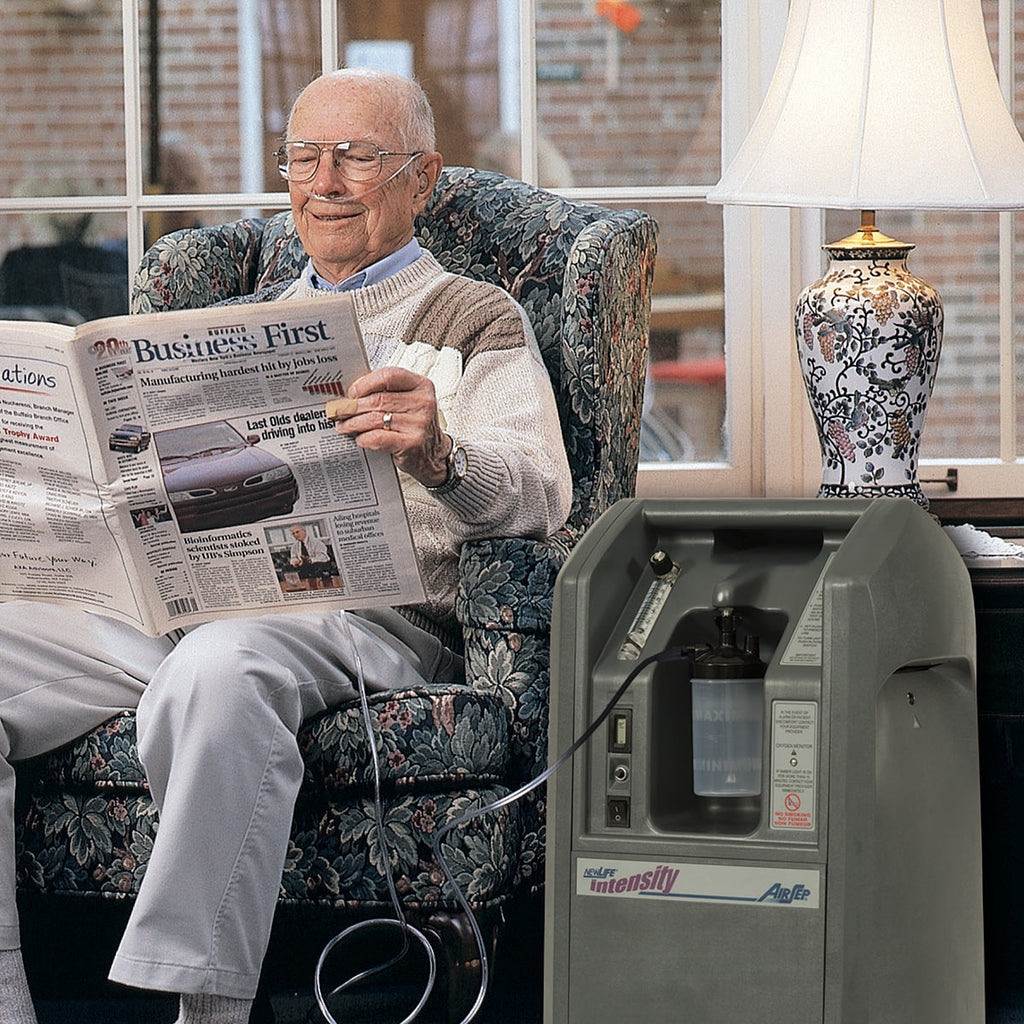 Man reading a newspaper next to an oxygen concentrator in a home setting.