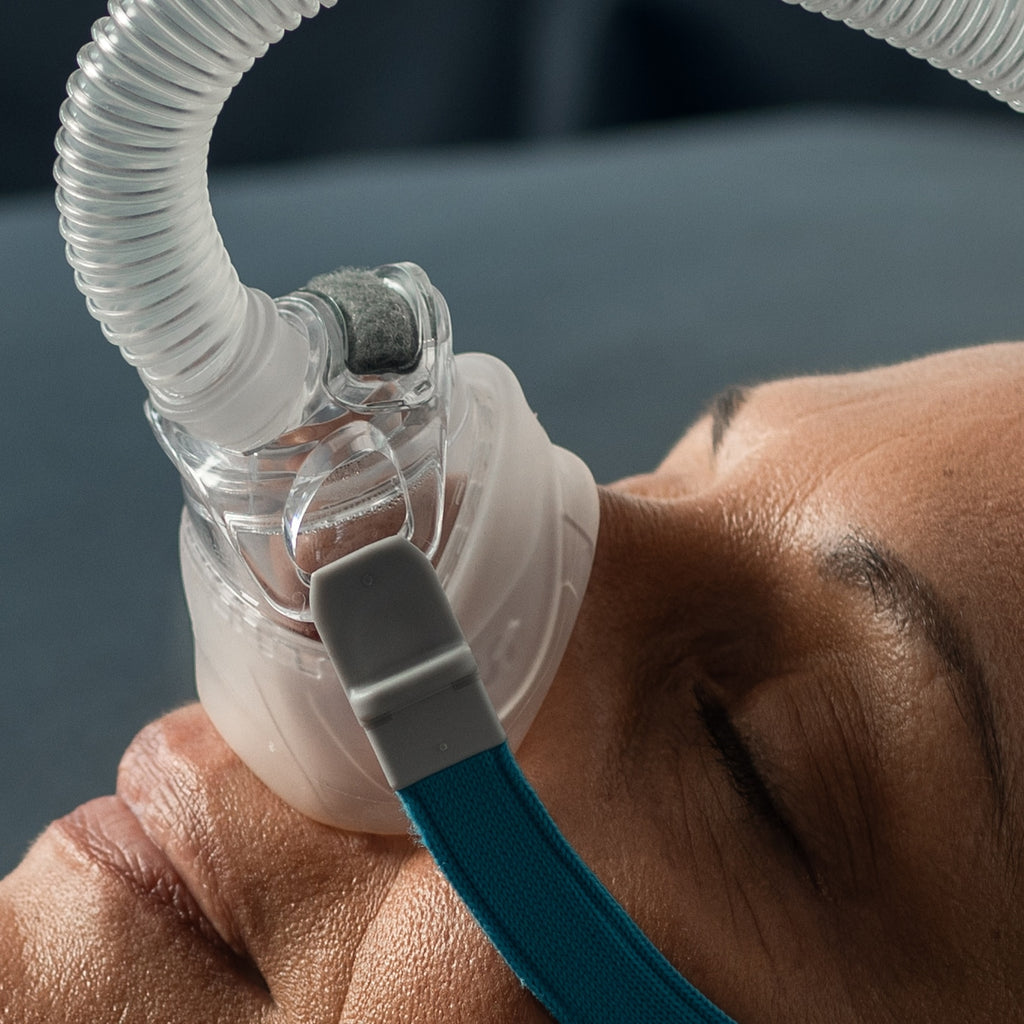 Person using a CPAP mask with hose and blue strap against a blurred background