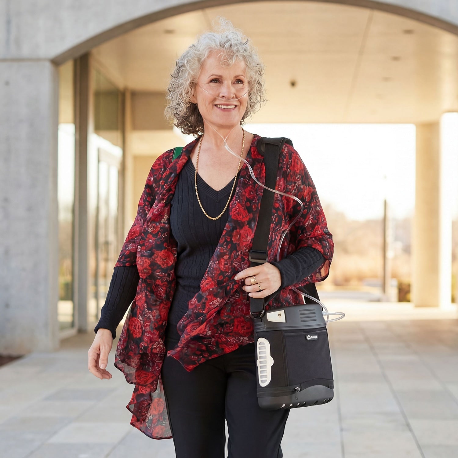Woman with a floral jacket and black bag containing an Oxlife 2 Portable Oxygen Concentrator walking outdoors.