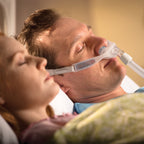 Man wearing philips respironics nuance pro gel nasal pillow mask sleeping next to women