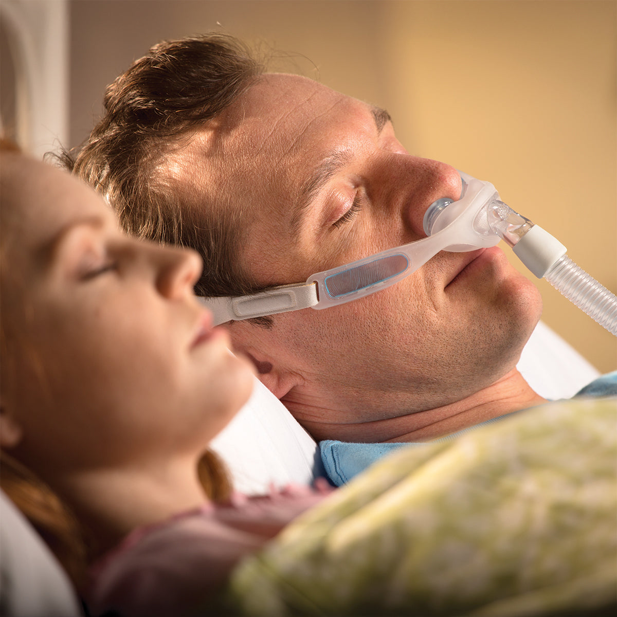 Man wearing philips respironics nuance pro gel nasal pillow mask sleeping next to women