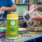 Snugell CPAP mask wipes container on a colorful tiled bathroom counter with a person using CPAP equipment.