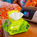 Green container of CPAP mask wipes  placed on a wooden surface with a colorful blanket in the background.