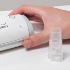 Hand holding a small white CPAP next to a cpap hose connector 