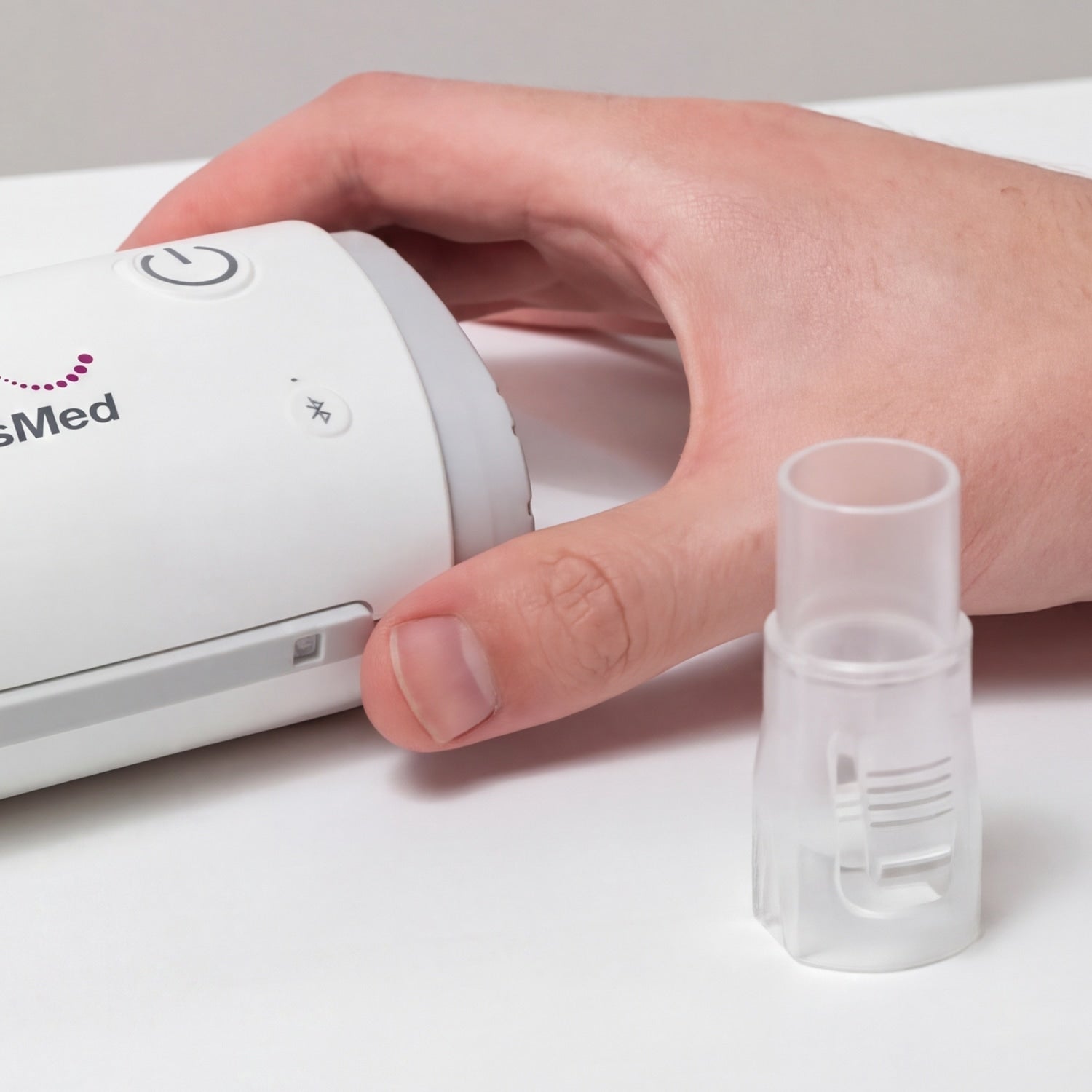 Hand holding a small white CPAP next to a cpap hose connector 