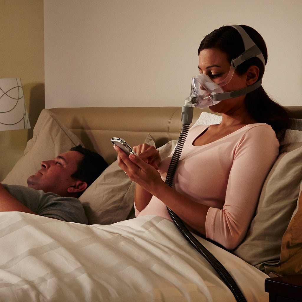 Woman using a CPAP machine while lying in bed with a man.