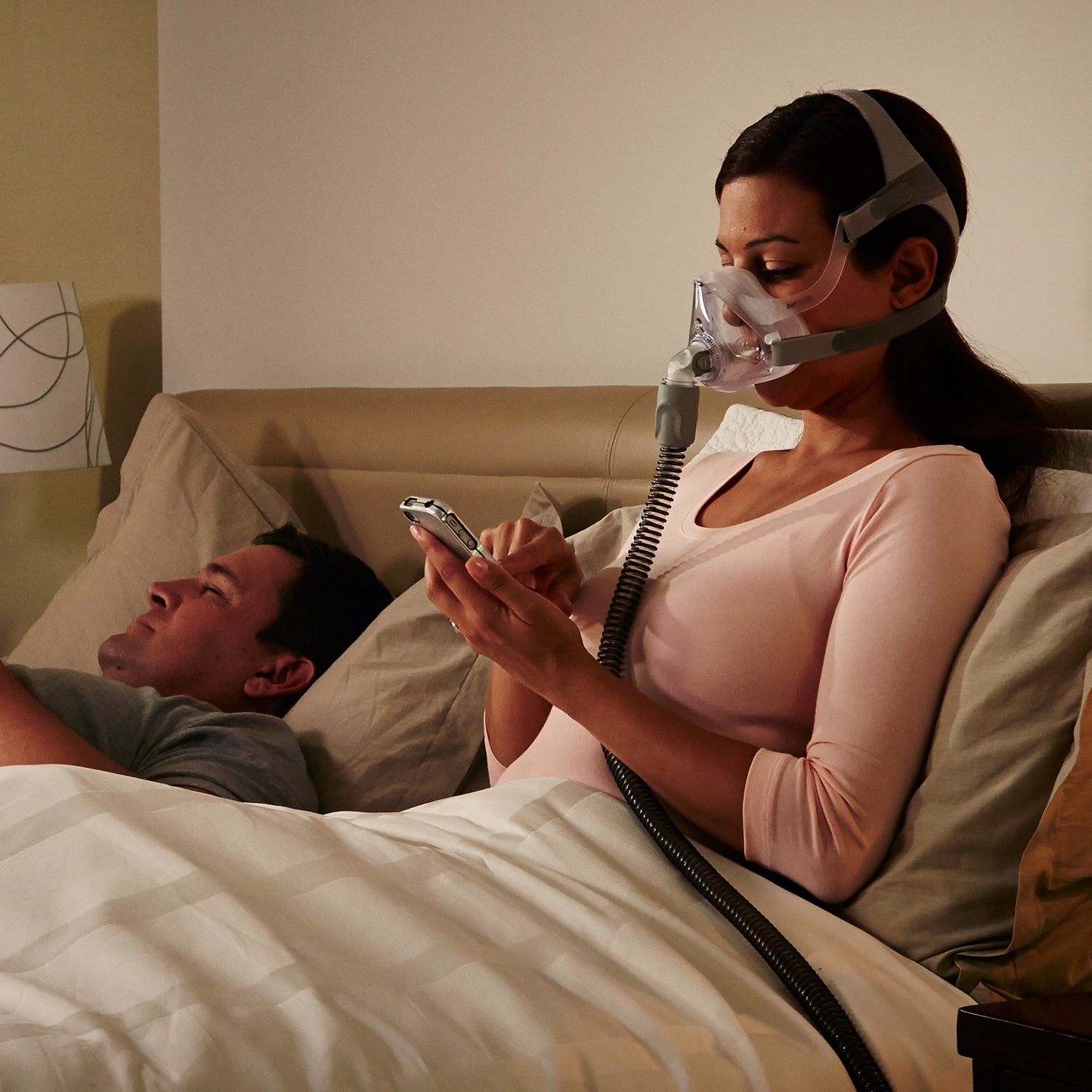 Woman using a CPAP machine while lying in bed with a man.